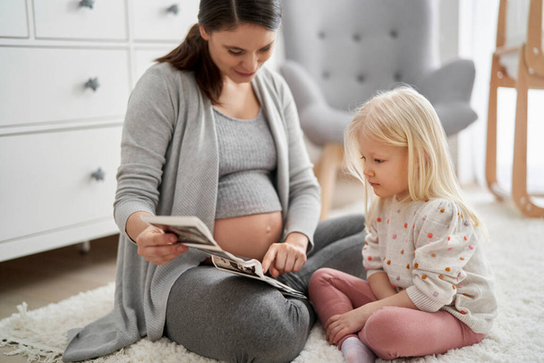 Kaukasierin in fortgeschrittener Schwangerschaft untersucht Ultraschalluntersuchung mit ihrer Tochter im Grundschulalter  - Foto, Bild