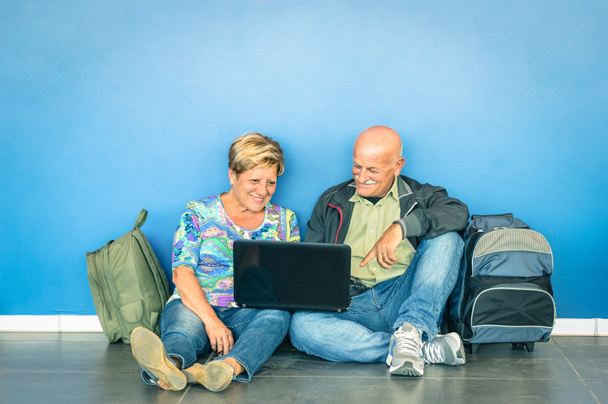 Casal sênior feliz sentado no chão com laptop esperando por um voo no aeroporto - Conceito de idosos ativos e interação com novas tecnologias - Estilo de vida de viagem sem limitação de idade
 - Foto, Imagem