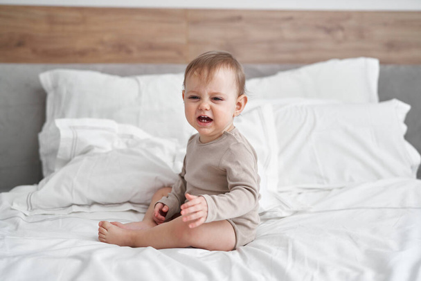 Kafkasyalı küçük bir kız bebek yatakta oturup ağlıyor. - Fotoğraf, Görsel