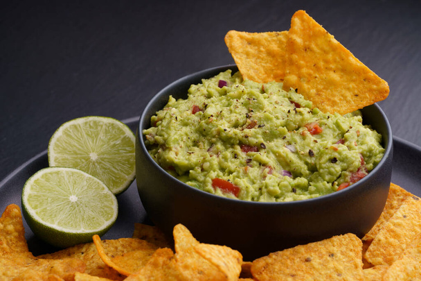 Guacamole dip with tortilla chips or nachos and lime on a black background - Valokuva, kuva