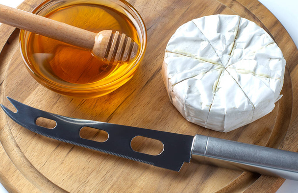 Camembert di formaggio con coltello e miele a bordo per il taglio, su fondo bianco. - Foto, immagini