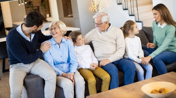 Modern evdeki kanepeye oturup televizyon izleyen çok nesilli bir aile. - Fotoğraf, Görsel