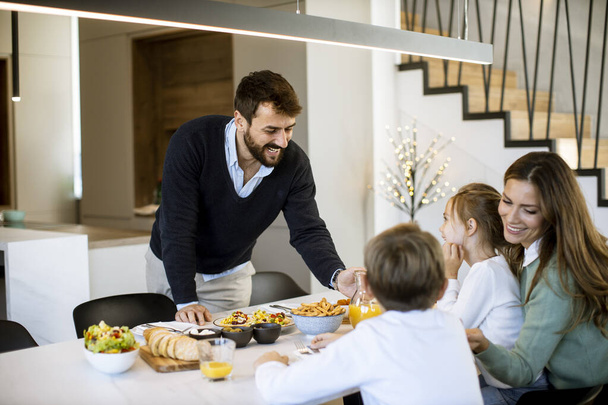 Молода щаслива сім'я розмовляє під час сніданку за обіднім столом в квартирі
 - Фото, зображення