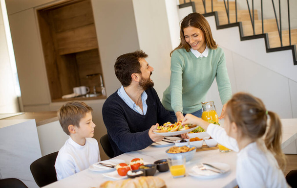 Fiatal boldog család beszél, miközben reggelizik az étkezőasztalnál a lakásban - Fotó, kép