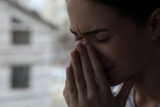 Traurige junge Frau weint am Fenster drinnen, Nahaufnahme mit Platz für Text. Konzept der Einsamkeit - Foto, Bild
