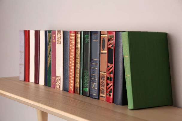 Wooden shelf with different books on light wall - Foto, imagen