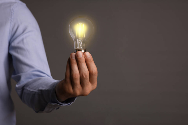 Glow up your ideas. Closeup view of man holding light bulb on grey background, space for text - Foto, immagini