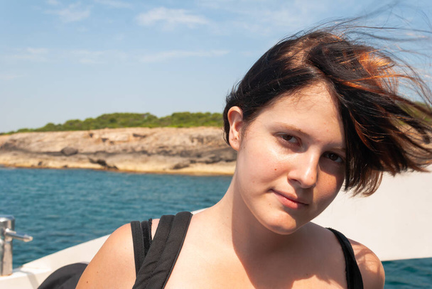 Młoda kobieta z czarnymi pomarańczowymi włosami patrząca w kamerę stojąc na statku na Morzu Śródziemnym, Majorka - Zdjęcie, obraz