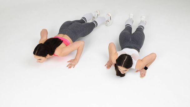 Two sportswomen doing push-ups from the floor on a white background in the studio - Foto, afbeelding
