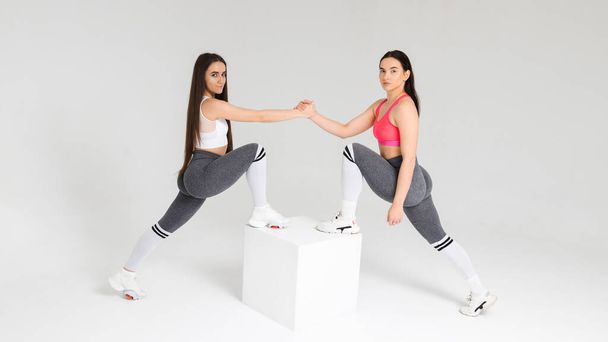 Dwie kobiety z siłowni podają sobie rękę, stojąc na kostce w studio. Koncepcja pracy zespołowej - Zdjęcie, obraz