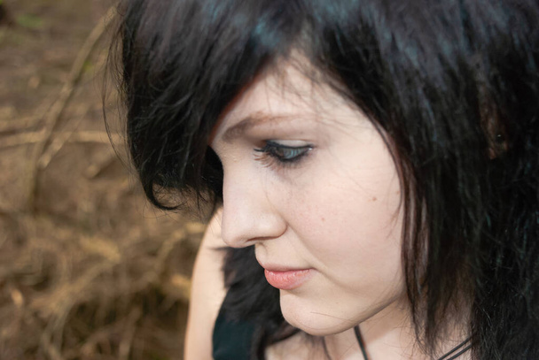 Punk emo κορίτσι, νεαρός ενήλικας με μαύρα μαλλιά και eyeliner, κοιτάζοντας μακριά, δάσος, κοντινό πλάνο, οριζόντια - Φωτογραφία, εικόνα