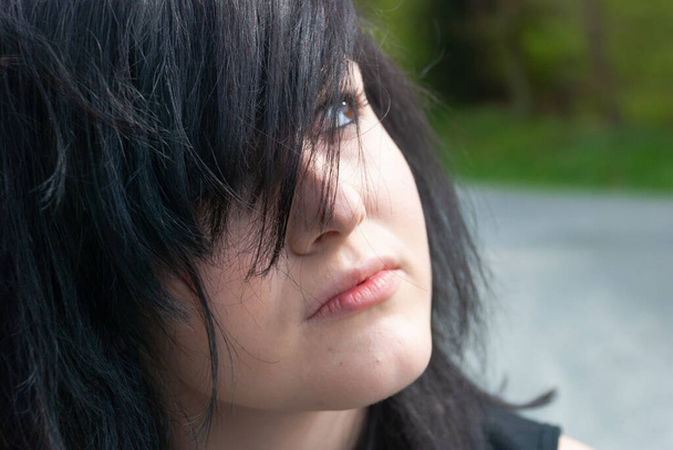 Панк-эмо девушка, молодой взрослый человек с черными волосами и подводкой для глаз, смотрит вверх, на улице, горизонтальный, крупный план - Фото, изображение