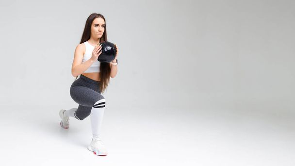 Jonge atletische vrouw doet lunges met een medicijnbal in haar handen. - Foto, afbeelding