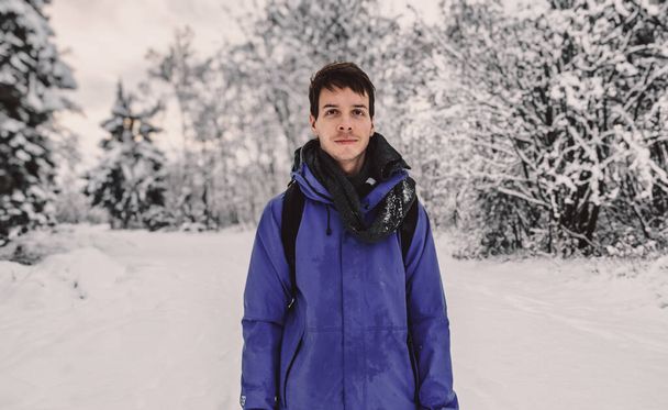 Junger erwachsener Mann mit braunen kurzen Haaren steht im Winter in Norwegen vor einer wunderschönen Schneelandschaft, trägt eine blaue Regenjacke, blickt in die Kamera, Norwegen - Foto, Bild