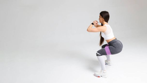 Αθλητική κοπέλα που κάνει κοιλιακούς με μπάντα αντίστασης γυμναστικής. Αθλητικές ασκήσεις μιας νεαρής γυναίκας σε λευκό φόντο - Φωτογραφία, εικόνα