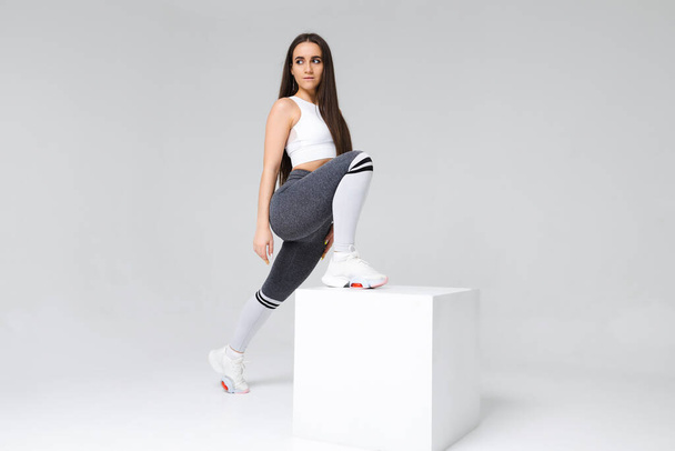 Young fitness woman with slender body poses at cube in studio - 写真・画像