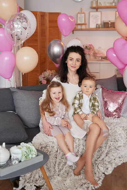 Valentine's Day. International Day of Happiness. Studio apartment in loft style. Holiday decor. Mothers Day. Happy family mother, daughter and and son with flowers and balloons celebrate. - Photo, Image
