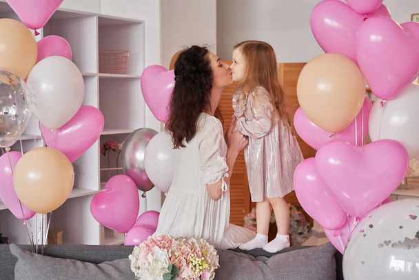 Valentine's Day. International Day of Happiness. Studio apartment in loft style. Holiday decor. Mothers Day. Woman mother and baby girl with balloons and flowers. Celebration - Photo, Image