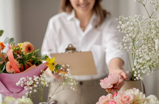 happy woman with clipboard and flowers at studio - Photo, image