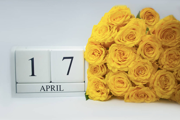 Calendrier en bois le 17 avril et roses jaunes sur fond blanc.  - Photo, image