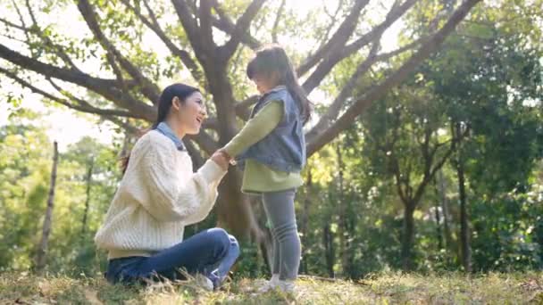 nuori aasialainen äiti rentouttava tyttären kanssa ulkona puistossa - Materiaali, video