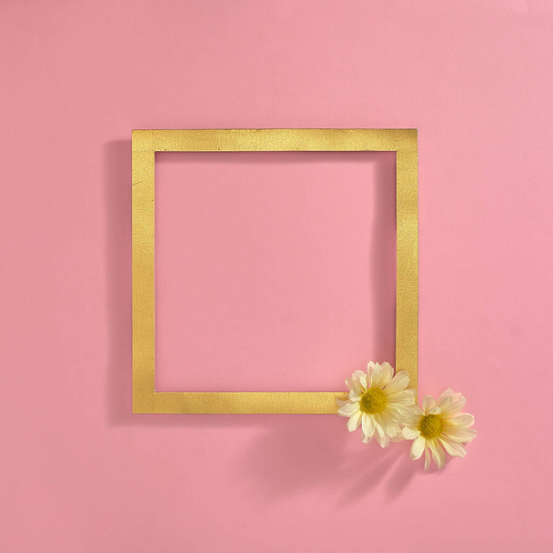 In de hoek van het gouden frame, twee witte bloemen op een pastelroze achtergrond. Tekstruimte. Bovenaanzicht. Minimale stijl. - Foto, afbeelding