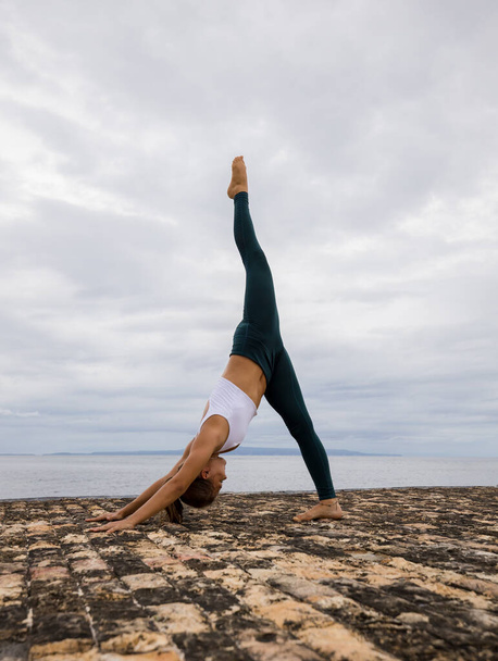 Гнучка молода жінка практикує гімнастичні вправи. Парватасана, поза гори. Одна нога вверх. Сильне тіло, прямо назад. Здоровий спосіб життя. Хмарове тло. Відступ йоги. Копіюю простір. Балі (Індонезія) - Фото, зображення