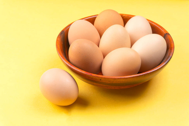Ξύλινο μπολ με αυγά κοτόπουλου σε κίτρινο φόντο, κοντινό πλάνο  - Φωτογραφία, εικόνα