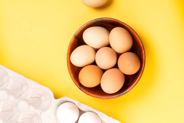 Wooden bowl of chicken eggs on yellow background, closeup shot  - Photo, Image