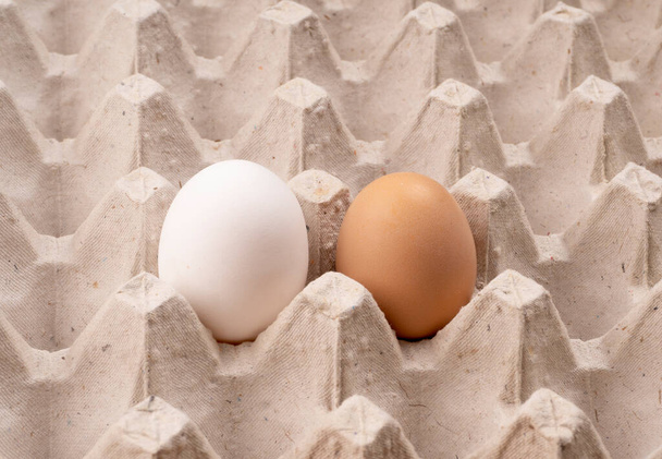 Karton tepside seçici odaklı beyaz ve kahverengi organik yumurtalar. Sağlıklı protein kahvaltısı için. Keto diyeti. Geleneksel Paskalya yemeği için iki tavuk yumurtası. - Fotoğraf, Görsel