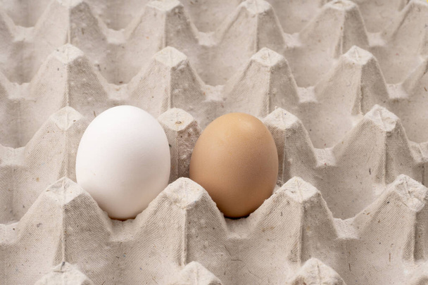 Белые и коричневые сырые органические яйца с выборочным фокусом в картонной ложе. Ингредиент для здорового белкового завтрака. Кето диета. Два яйца птицы для традиционного пасхального блюда - Фото, изображение