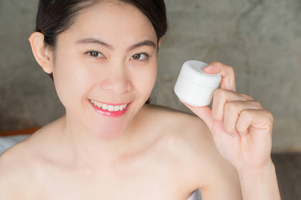 Portrait de jeune femme asiatique tenant le récipient de crème d'emballage dans sa main. Conceptuel de beauté et cosmétique. - Photo, image