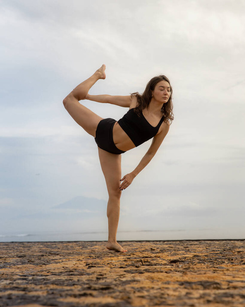 Sunrise ioga e alongamento. Mulher caucasiana atraente praticando ioga, de pé em Natarajasana, Senhor da Dança Pose. Balanceamento, costas dobrando asana. Exercício na praia. Bali, Indonésia - Foto, Imagem