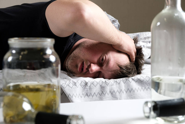 V posteli leží opilý muž a drží si ruce u hlavy. Kocovina, alkoholické delirium. - Fotografie, Obrázek