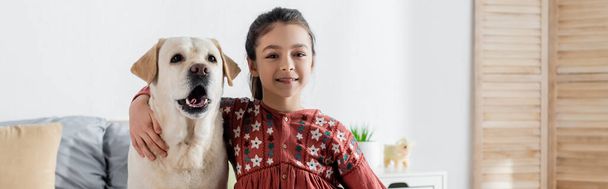 positive girl hugging labrador dog and looking at camera, banner - Foto, imagen