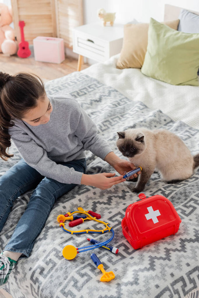 magas látószögű kilátás a játékfecskendővel macskának injekciót beadó lányra - Fotó, kép