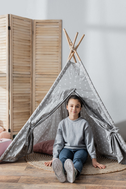 full length view of happy girl sitting on floor in wigwam - Photo, Image