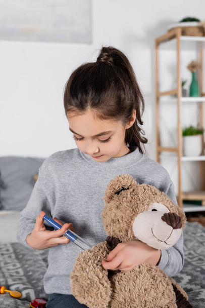 brunette preteen girl making injection to teddy bear with toy syringe - Foto, Bild