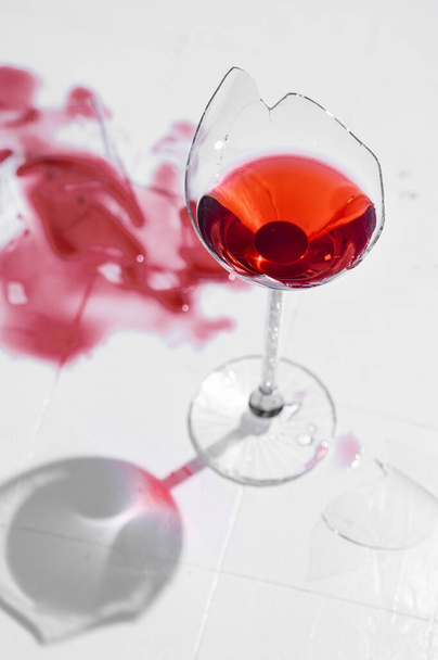 Broken glass with red wine on a table with white tiles - Foto, Bild