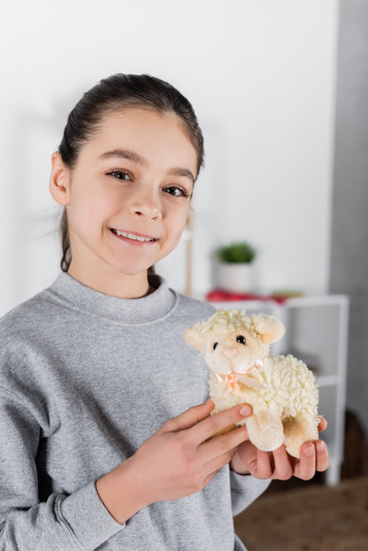 smiling girl showing toy lamb and looking at camera  - 写真・画像