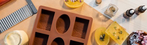 Vista superior do molde de silicone perto de sabão artesanal, flores e cortador na mesa, banner  - Foto, Imagem