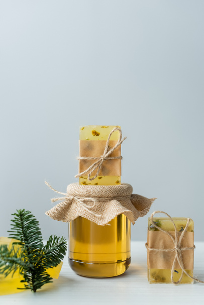 Jabón hecho a mano en tarro con miel cerca de rama de abeto sobre fondo gris  - Foto, Imagen