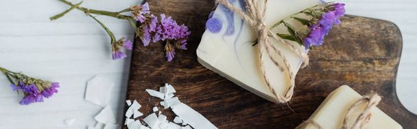 Horní pohled na řemeslnou mýdlovou tyč s květinami na řezací desce na stole, banner  - Fotografie, Obrázek