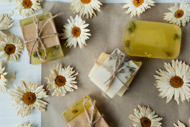 Κάτοψη χειροποίητων σαπουνιών κοντά σε στεγνά λουλούδια σε χαρτί χειροτεχνίας  - Φωτογραφία, εικόνα