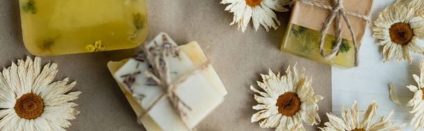 Vista dall'alto di fiori di camomilla secchi vicino alle saponette su carta artigianale, banner  - Foto, immagini