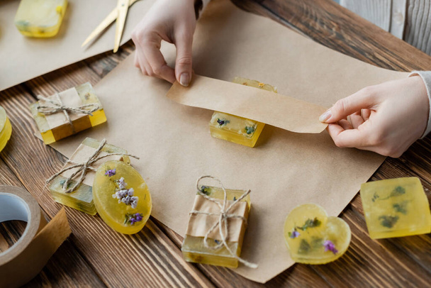 high angle view of craftswoman packaging handmade soap with dry flowers at home  - Photo, Image