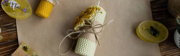 Top view of craft candles and soap with dry flowers on paper on wooden surface, banner  - Photo, Image
