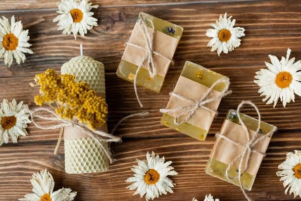 Top view of craft candle and soap near dry flowers on wooden surface  - Фото, зображення