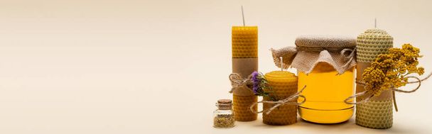 Velas artesanales con flores cerca del frasco con miel sobre fondo beige, pancarta  - Foto, imagen