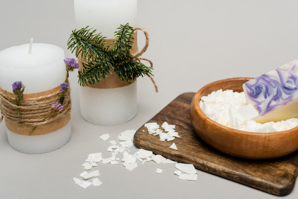 Bougies artisanales avec des plantes près de cire sèche sur planche de bois sur fond gris - Photo, image